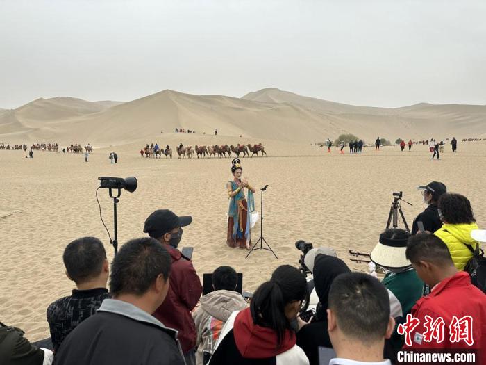 圖為2023年4月底，敦煌大漠“逐舞者”奧楠在鳴沙山月牙泉景區(qū)視頻直播，吸引游人圍觀。　馮志軍 攝